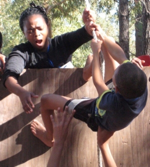 A trainer with Resilient Kids SA helps a camper over an obstacle