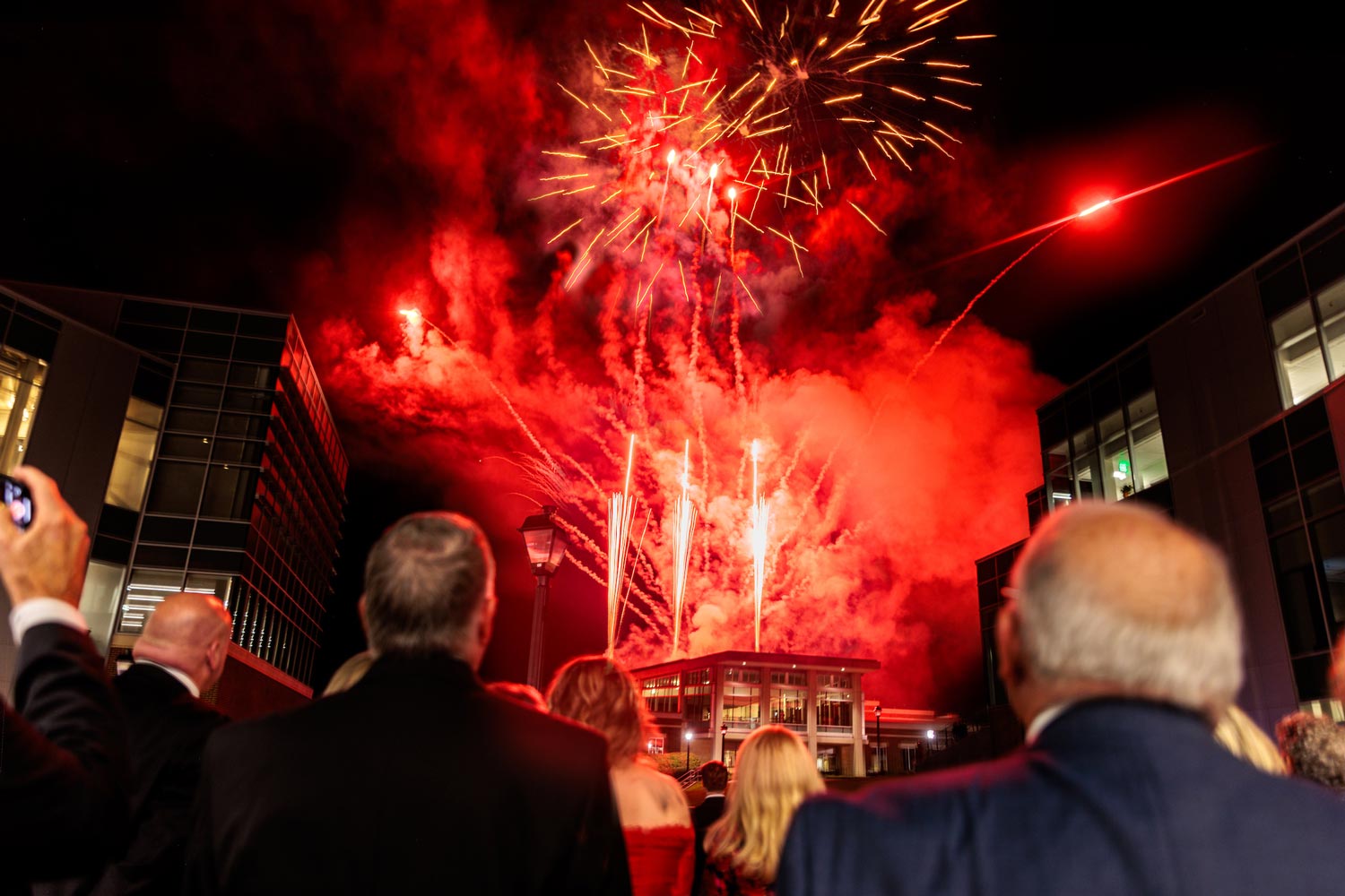 people stand watching fireworks over campus