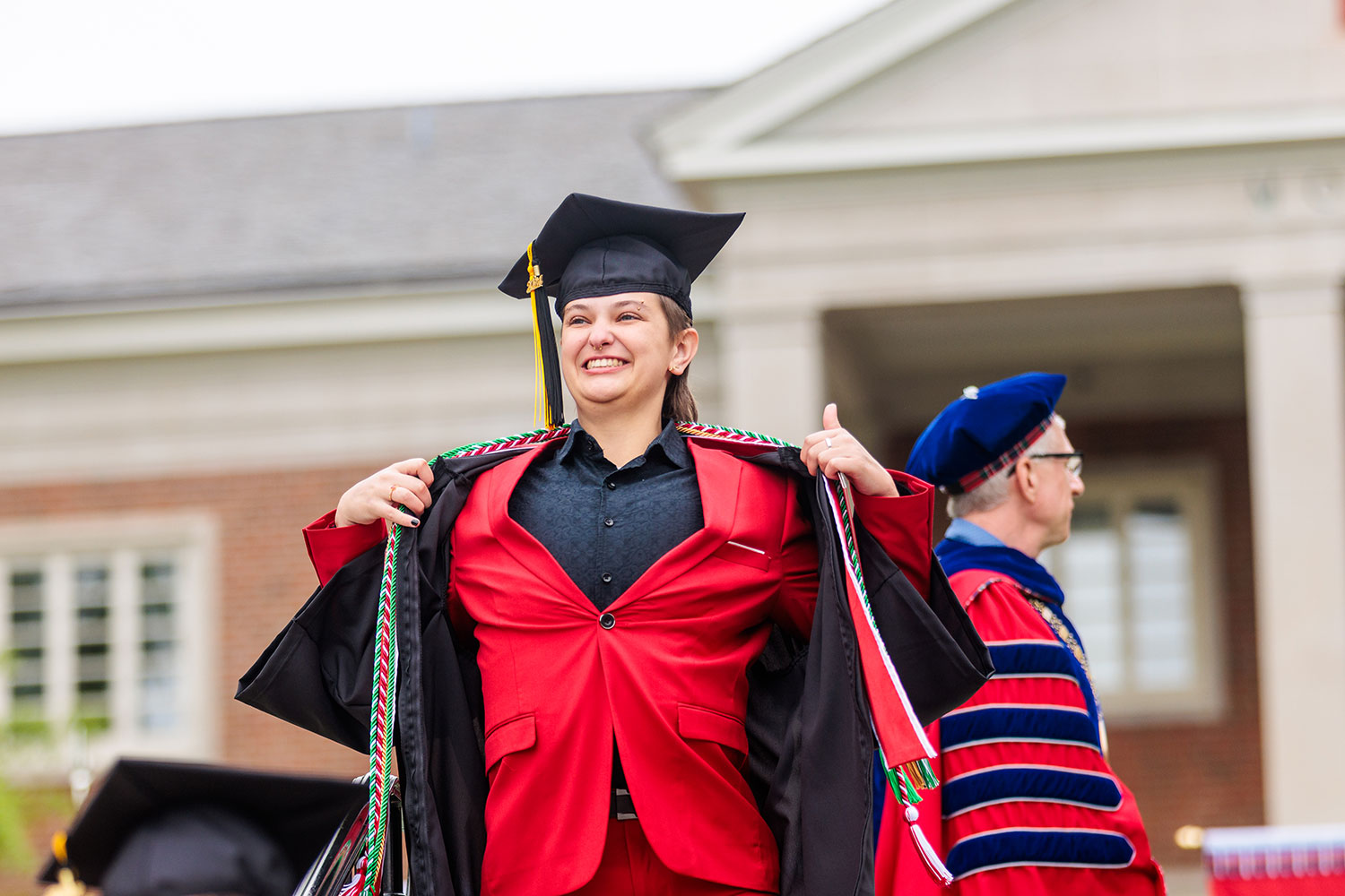 Student showing off a red suit underneath commencement regelia