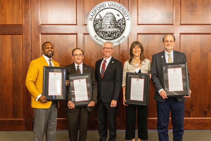 The president, three board members and a professor stand together and display their framed awards.