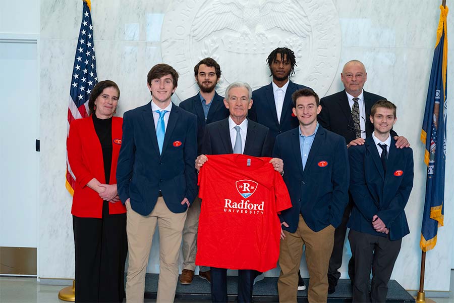 A group of business students, their professors and Federal Reserve Chairman Jerome Powell stand together after an annual competition in Washington, D.C. Powell holds up a red Radford T-shirt.