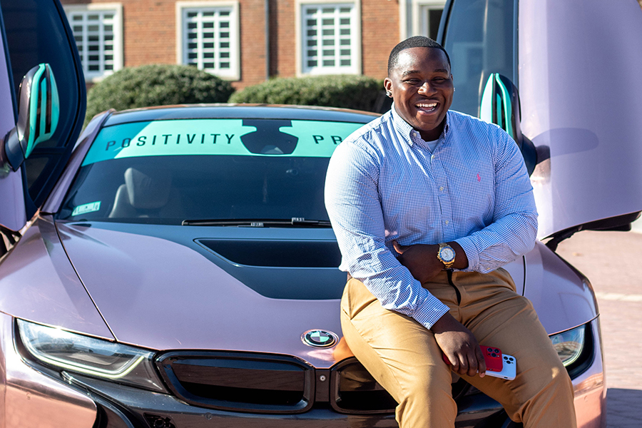 George Zama poses for a photo in front of his BMW on campus 
