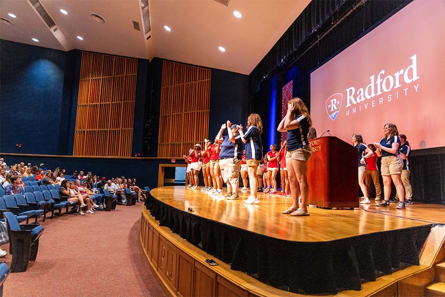 A group of student ambassadors dance onstage in front of incoming freshmen and transfer students.