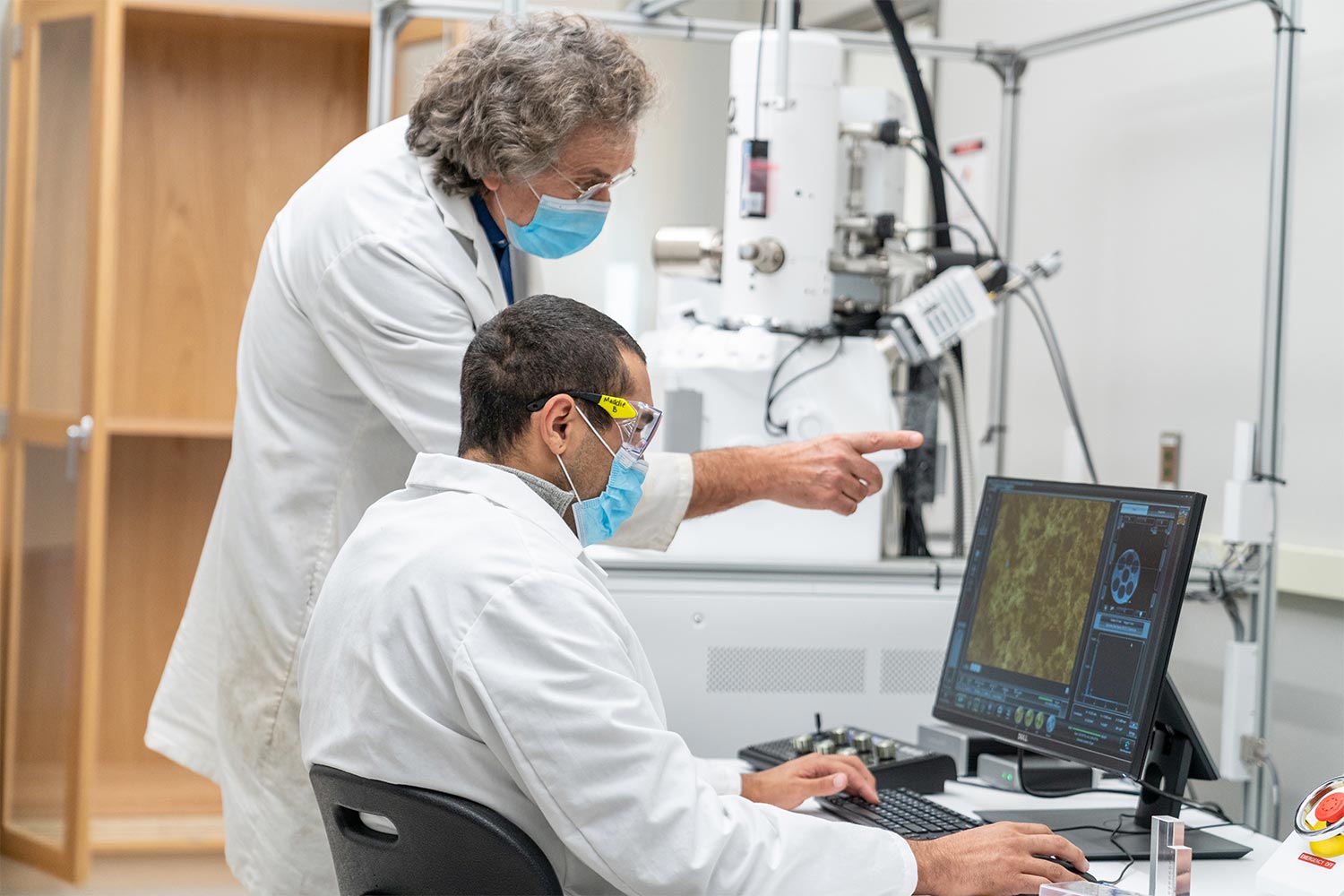 two men in white labcoats and masks looking at a computer screen