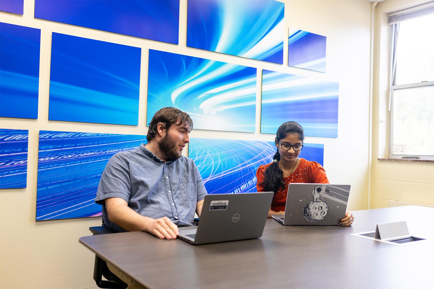 students with their laptops in front of a blue background wall