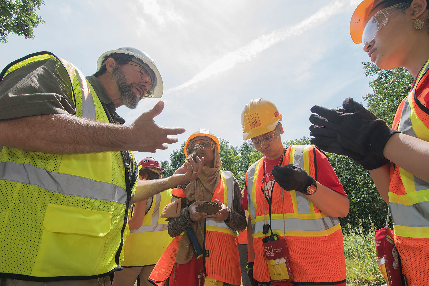 students in neon vests and hard hats huddled in a circle