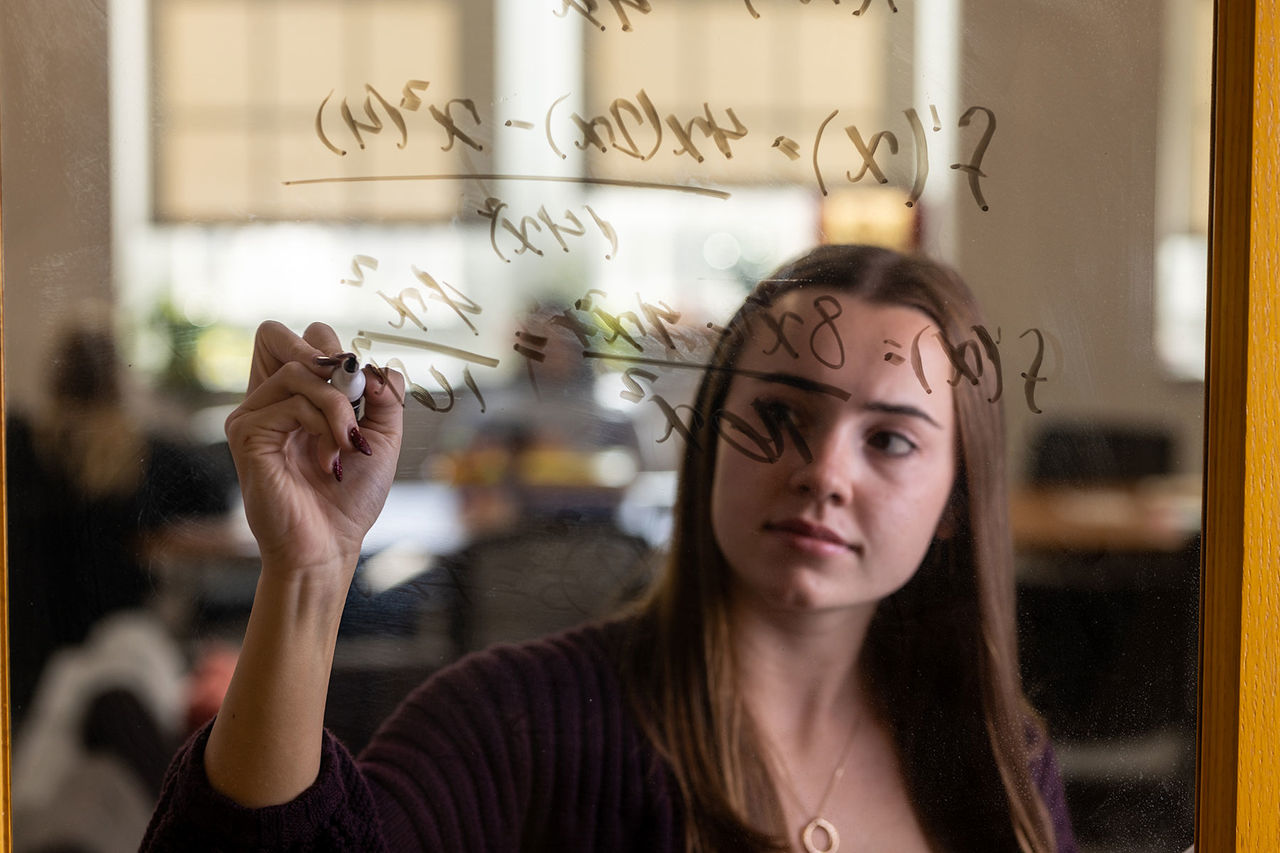 student writing equations on a transparent erasable board