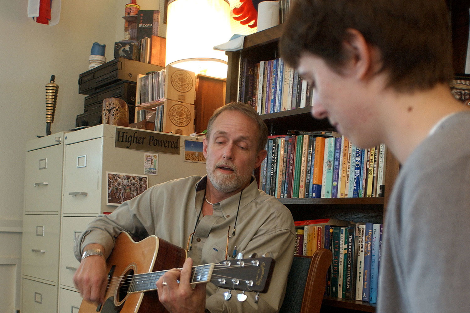 a male playing the guitar and another male listening