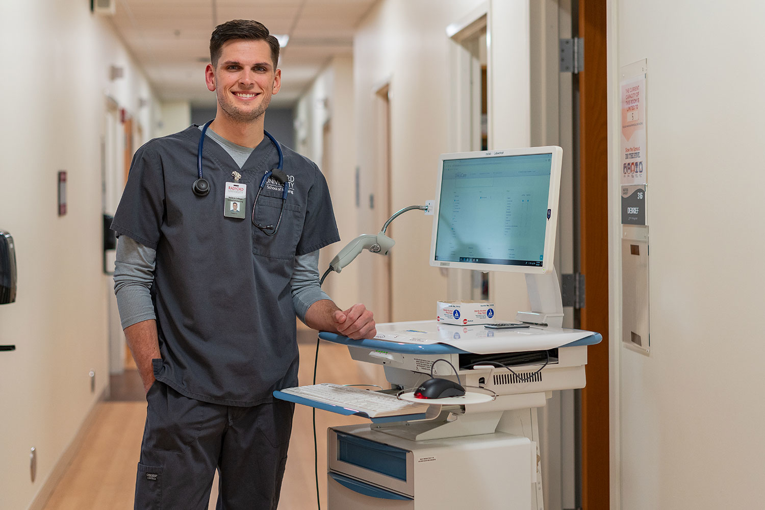 student in scrubs standing in front of a mobile computer