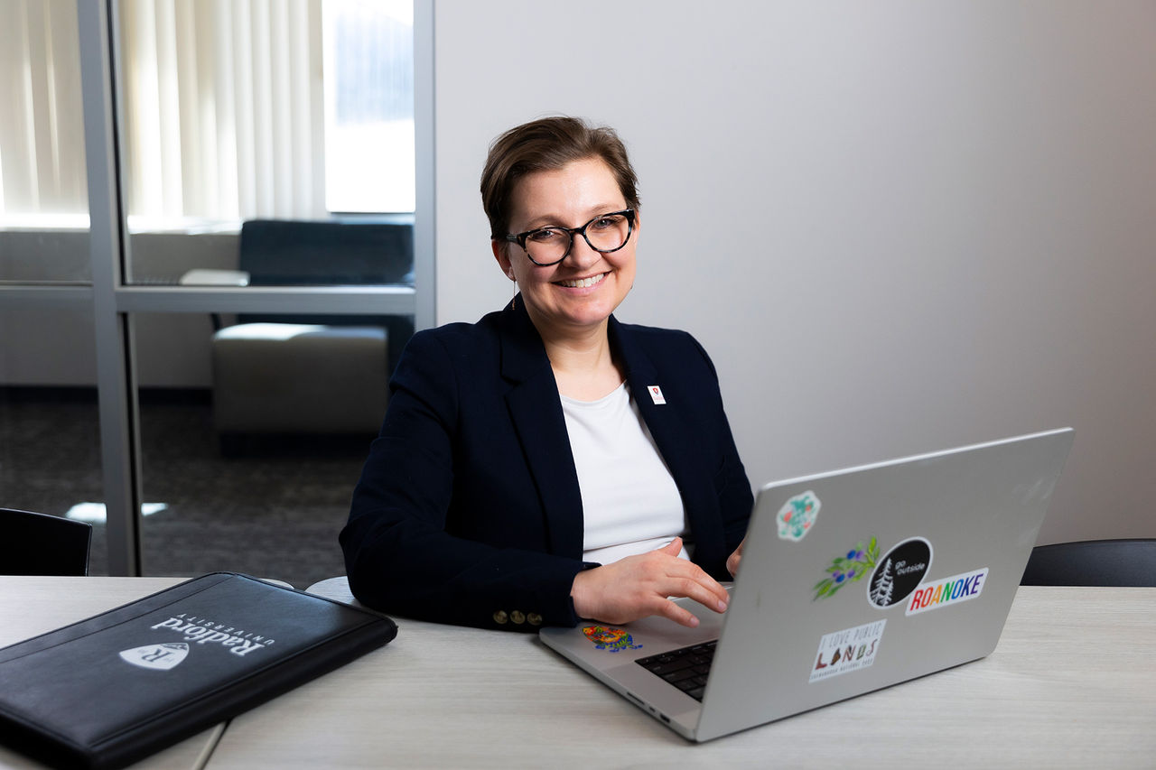 Rachel Rogers sitting at a desk on a laptop, smiling at the camera