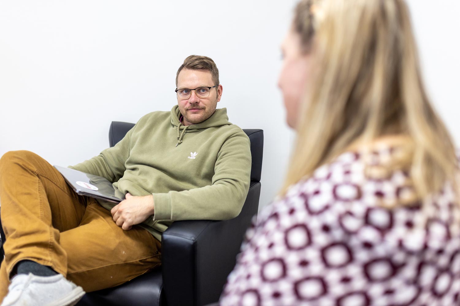 guy with laptop sitting in a chair looking at someone in a chair next to him