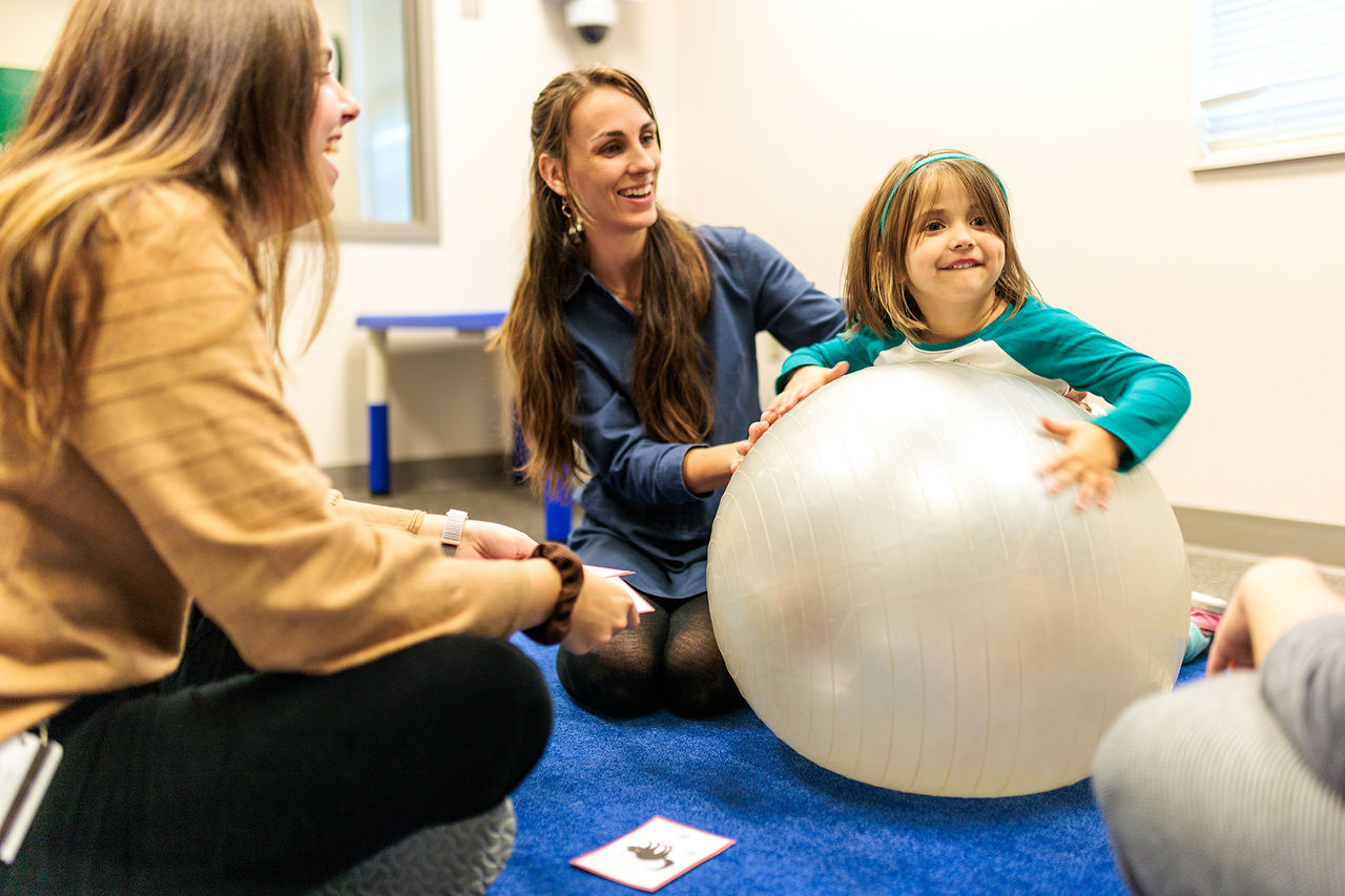 two adults helping a child using a yoga ball