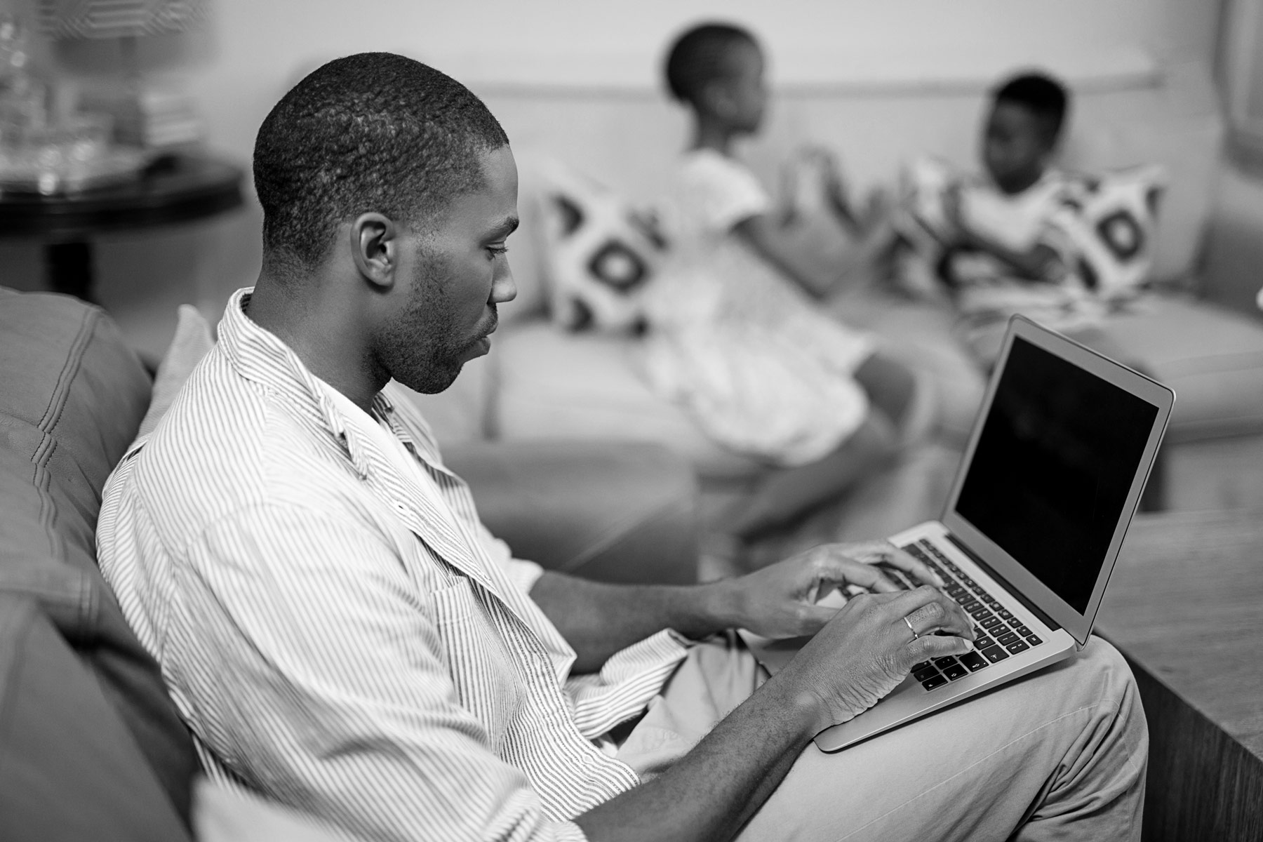 man on computer in living room with children in background
