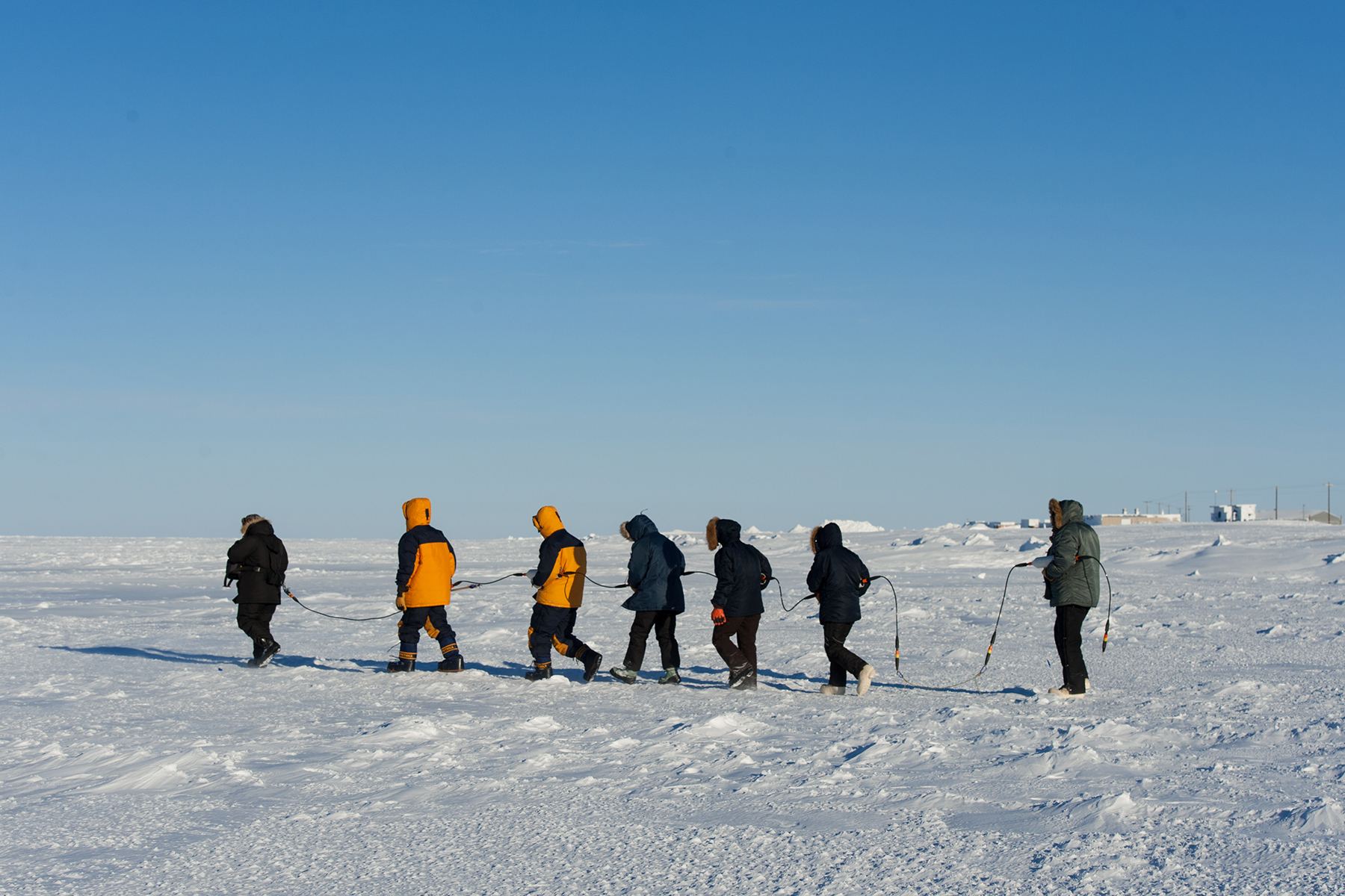 group of students holding a rope connecting them as they walk through a snowy terrain