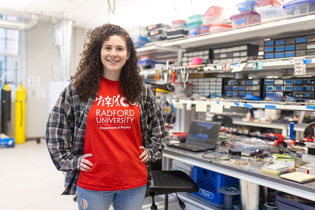student in a radford shirt standing in front of a desk covered in science materials