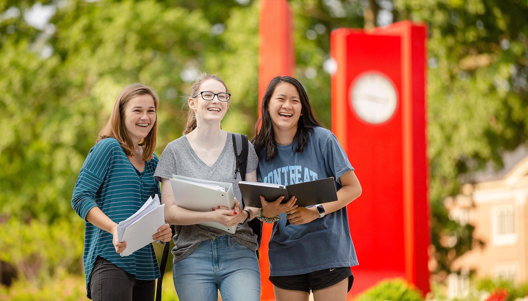 Three students smiling in front of Heth clocks.