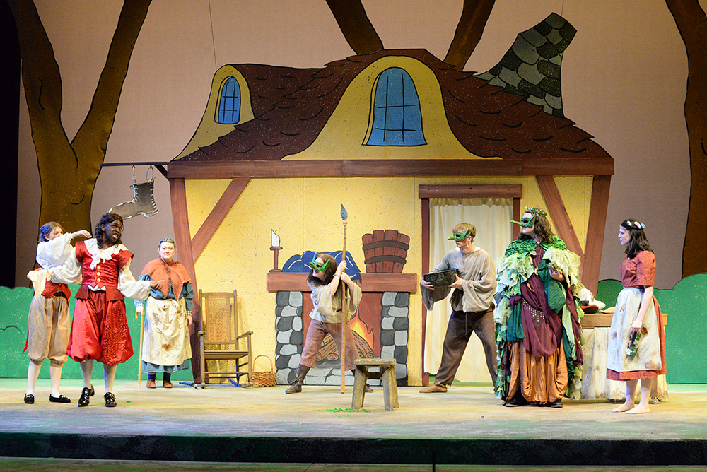 Performers in colorful fantasy costumes act on a cottage-themed stage during Radford University’s production of Lily and the Magic Stones.